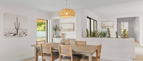 A dining area with a wooden table and chairs, a hanging light fixture, and framed artwork on the walls.