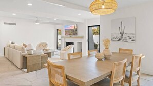 Un salon moderne avec un coin repas, comprenant une grande table en bois, des chaises en osier et un ventilateur de plafond.