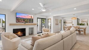 Un salon spacieux doté d’une cheminée, d’un grand téléviseur fixé au-dessus et d’un ventilateur de plafond moderne.