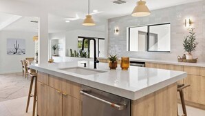 Une cuisine moderne dotée d’un grand îlot central, de luminaires suspendus et donnant sur l’espace repas.