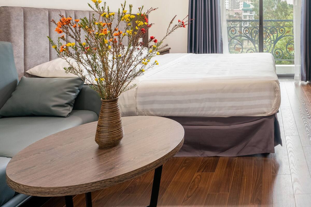Une chambre d’hôtel avec un lit, une petite table ronde ornée d’un vase de fleurs, un téléviseur et un bureau en bois.