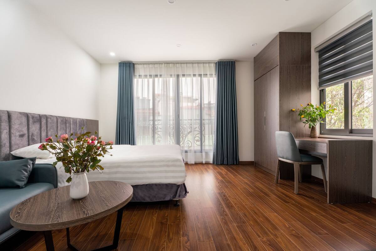 Une chambre d’hôtel moderne, équipée d’un lit, d’un bureau, d’une chaise, d’une petite table et d’un vase avec des fleurs.