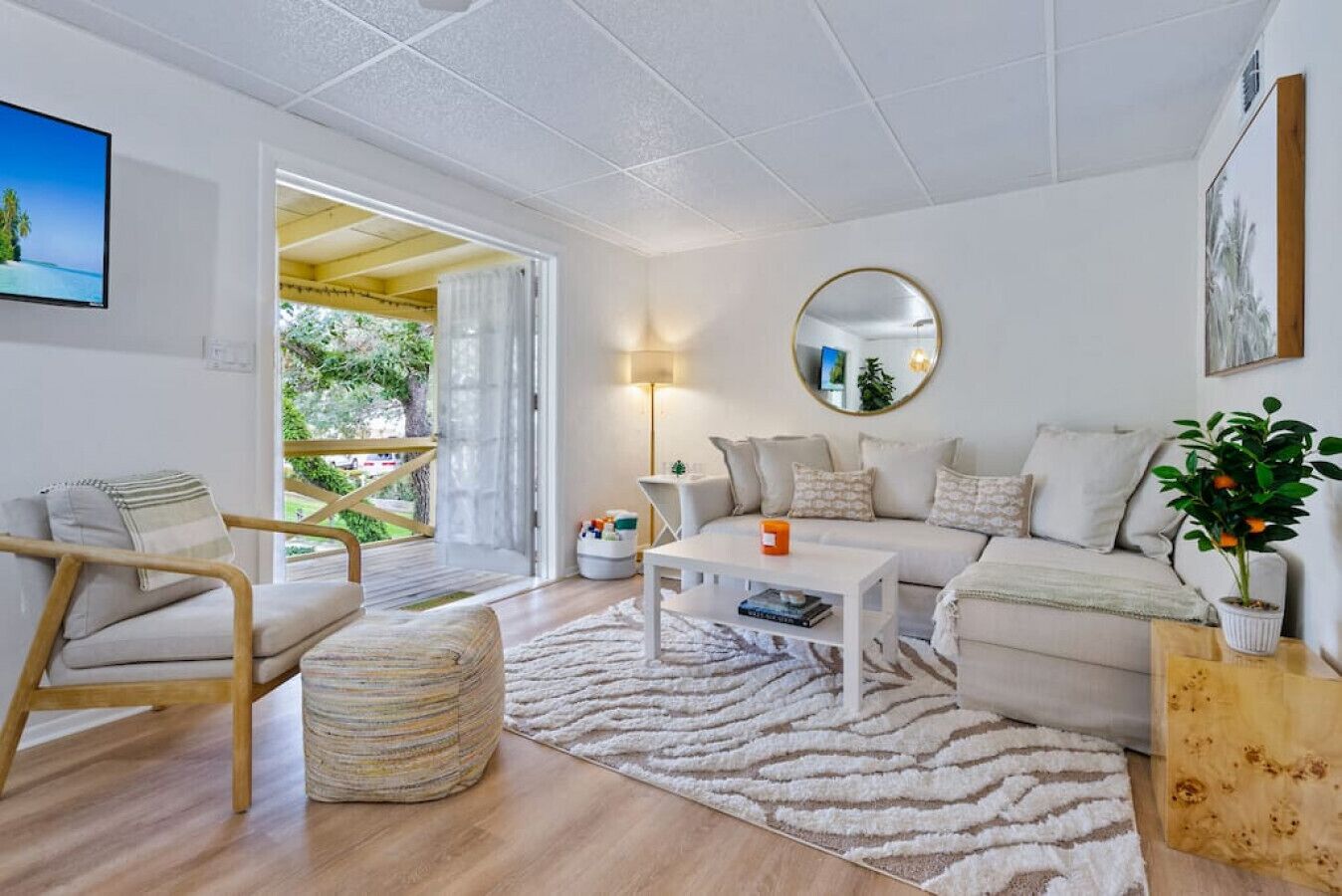 A modern living room with a sofa, coffee table, and a chair. There is a large mirror on the wall and a potted plant on a side table.