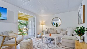 Un moderno salón con un sofá, una mesa de centro y una silla. Hay un espejo grande en la pared y una planta en maceta sobre una mesita auxiliar.