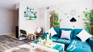 Ein modernes Wohnzimmer mit einem türkisfarbenen Sofa, einem Couchtisch und einem Gemälde von abstrakten Bäumen an der Wand.