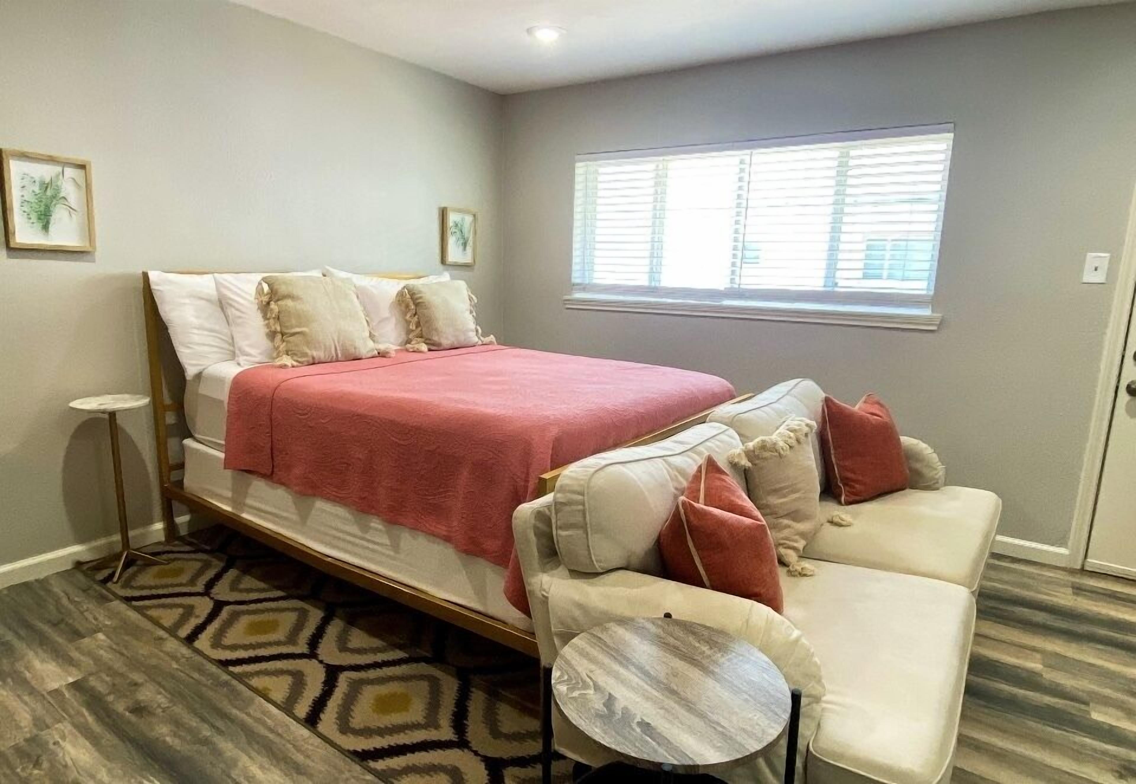 Une chambre à coucher avec un lit, un canapé, une petite table ronde et une fenêtre avec des stores.