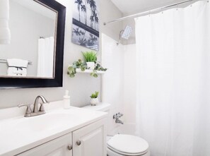 A modern bathroom with a white vanity, a large mirror, a toilet, and a shower curtain. - Paragon Apartments (Dallas)