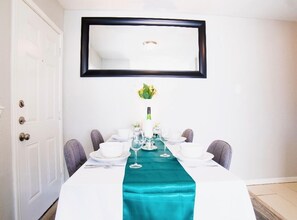 A dining area with a white table set for four, a teal runner, and a framed picture above the table. - Paragon Apartments (Dallas)