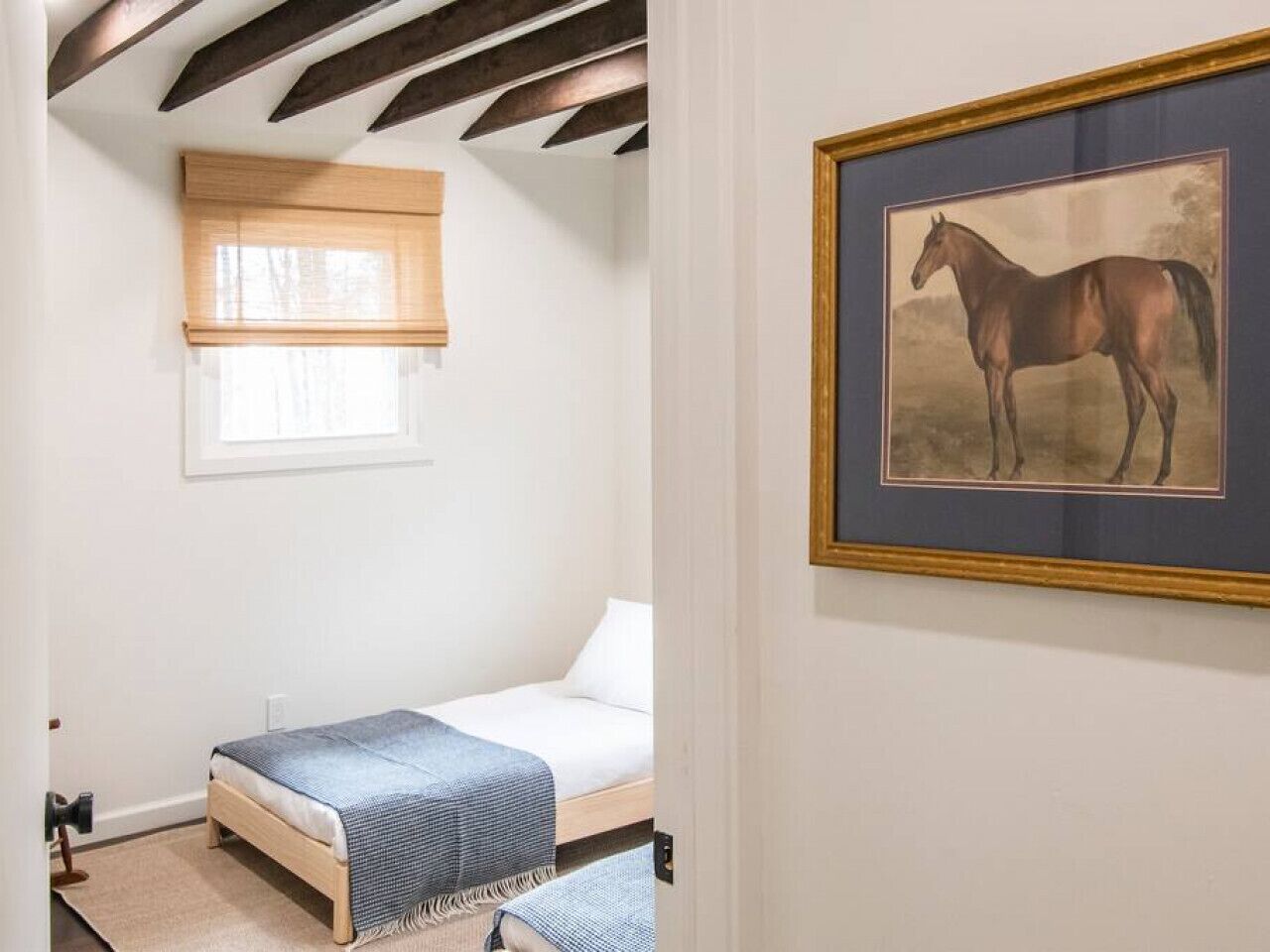 Une chambre à coucher avec un lit, une fenêtre avec un store et un tableau encadré accroché au mur.