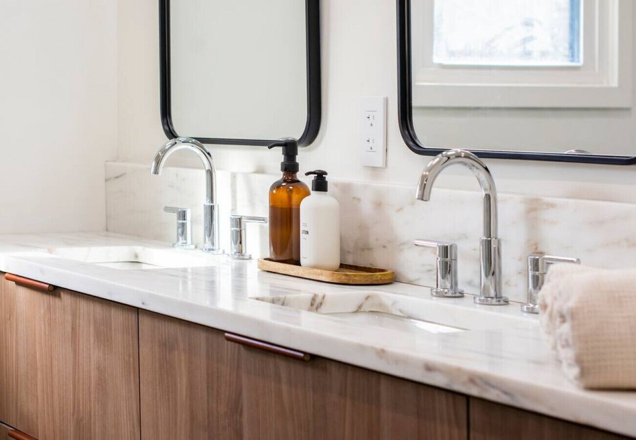 A bathroom with a double sink, two faucets, a soap dispenser, and a towel.