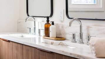 A bathroom with a double sink, two faucets, a soap dispenser, and a towel.