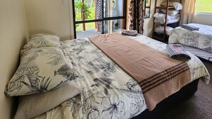 Quarto com duas camas, prateleira de madeira com toalhas dobradas e vista para o verde através de uma porta de vidro.