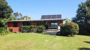 Uma casa moderna com painéis solares, um gramado bem cuidado e um arbusto grande.