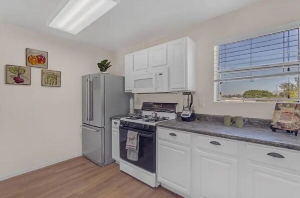 Kitchen features a gas stove, microwave, and oven, along with a refrigerator and window with blinds.