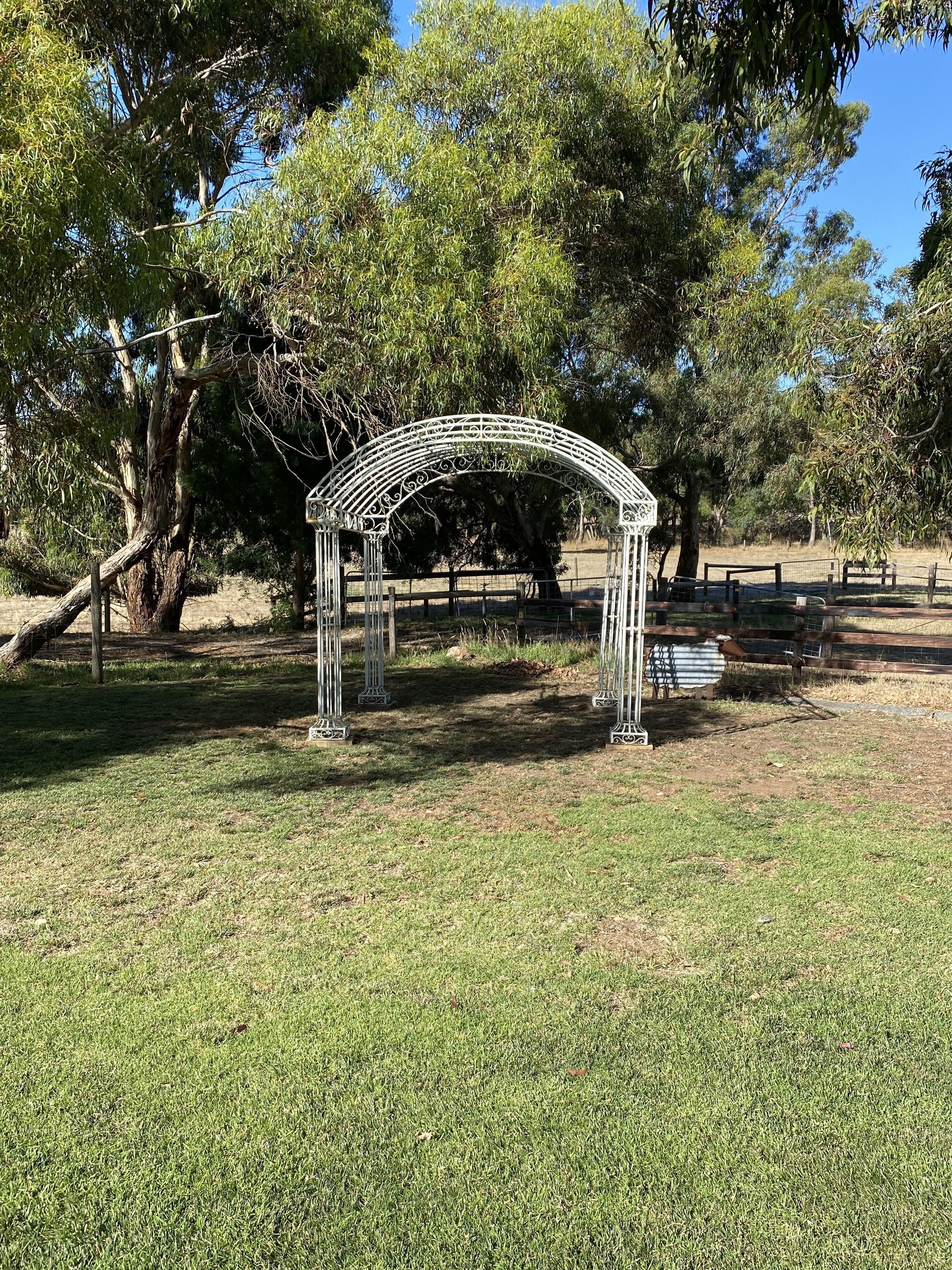 Un pabellón metálico en un parque con árboles y una valla al fondo.