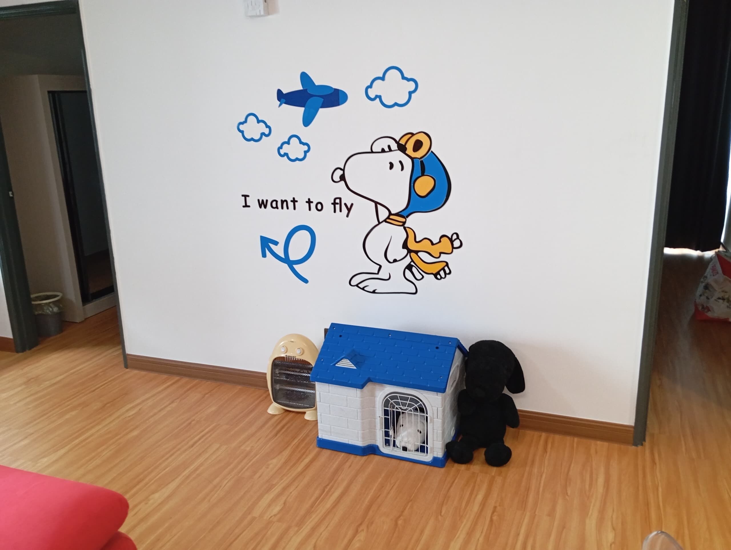 A wall with a Snoopy wall decal, a small blue house, and a black stuffed animal.