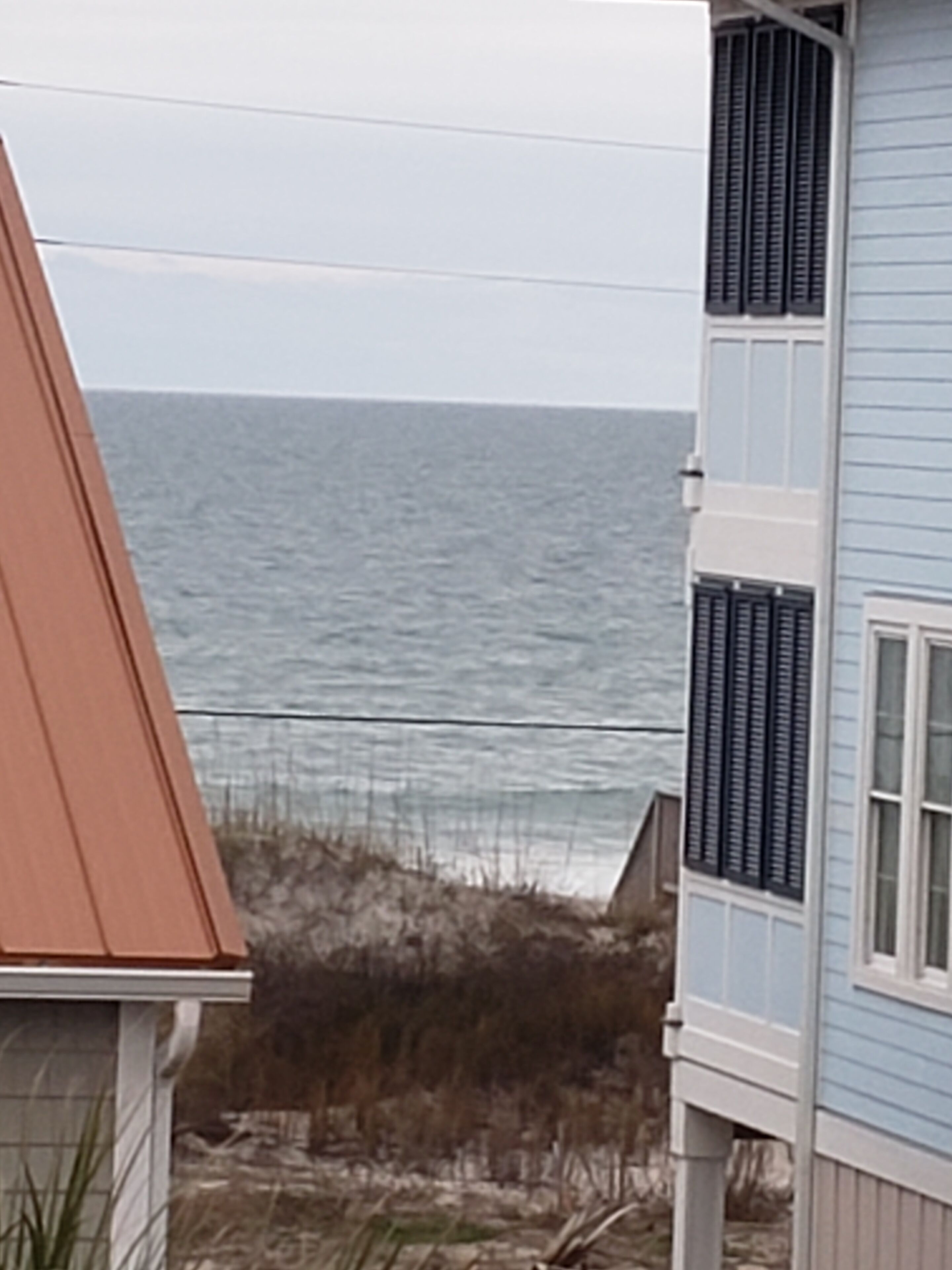 Une maison située sur la côte, dotée d’un toit en pente, d’un balcon et offrant une vue sur l’océan.