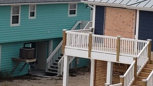 Un edificio costero con fachada azul, una terraza de madera y vista al océano.