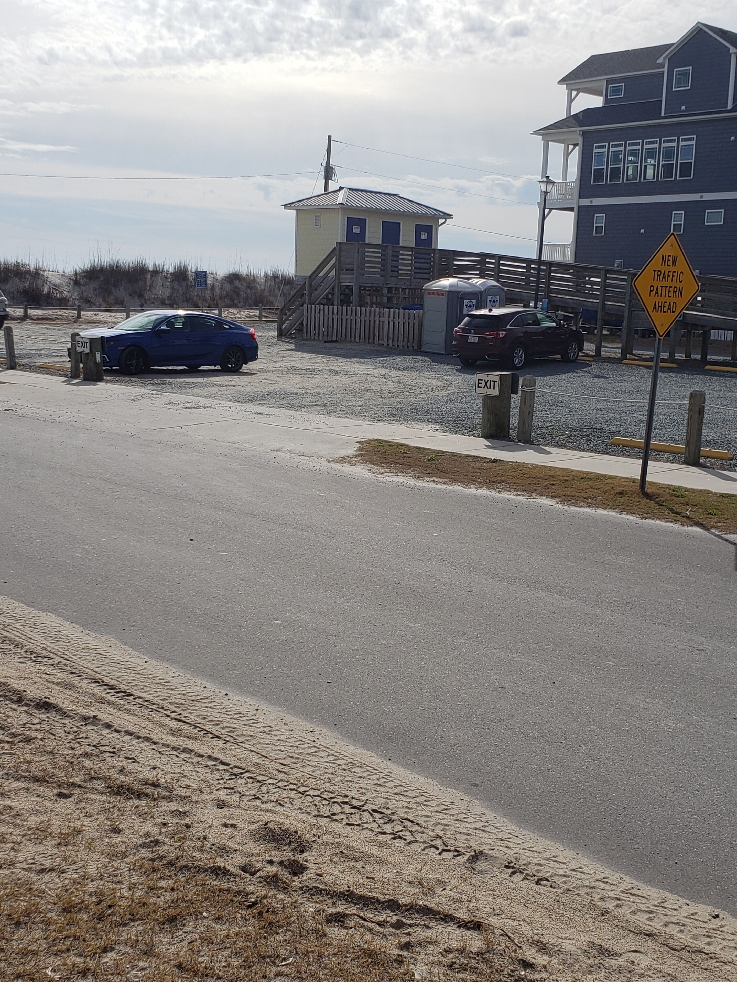 A parking area with a blue car and a trailer, a building with a ramp, and a 'NEW TRAFFIC PATTERN AHEAD' sign.