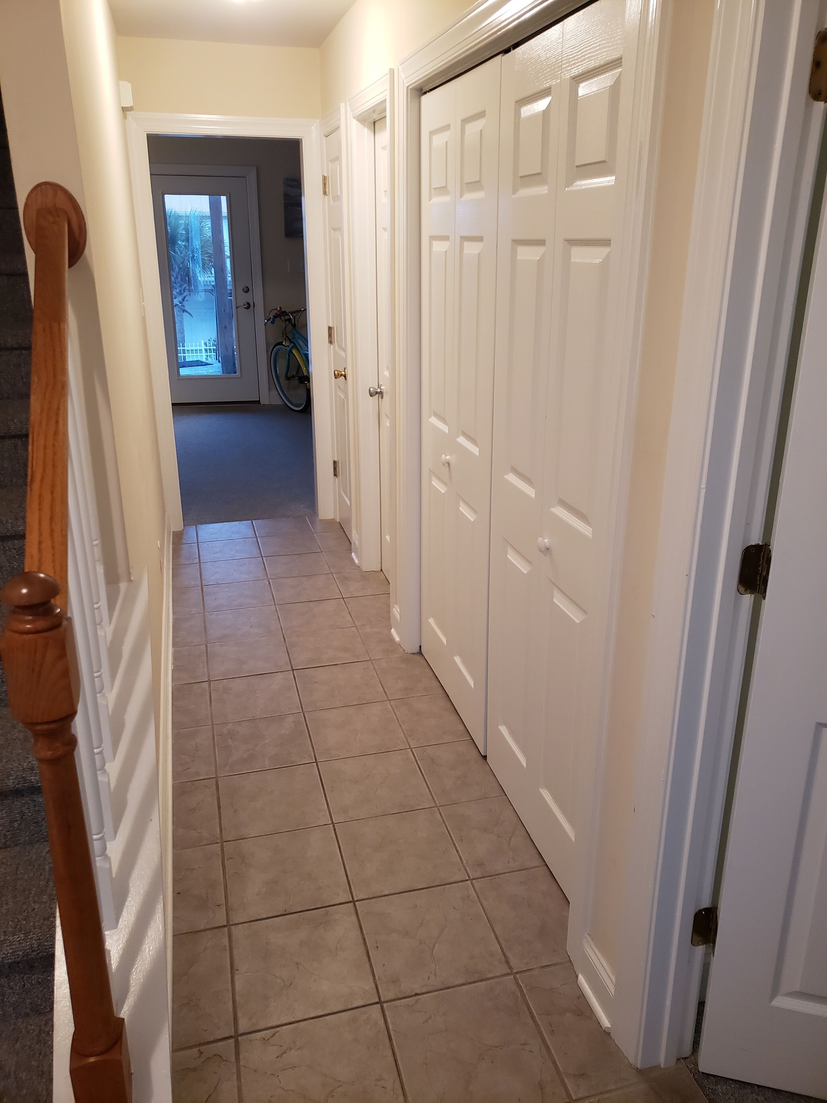 A hallway with beige tiled flooring, white doors, and a wooden staircase on the left.