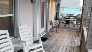 Una terraza de madera con sillas de plástico blanco y una mesa, con vista a una zona residencial.