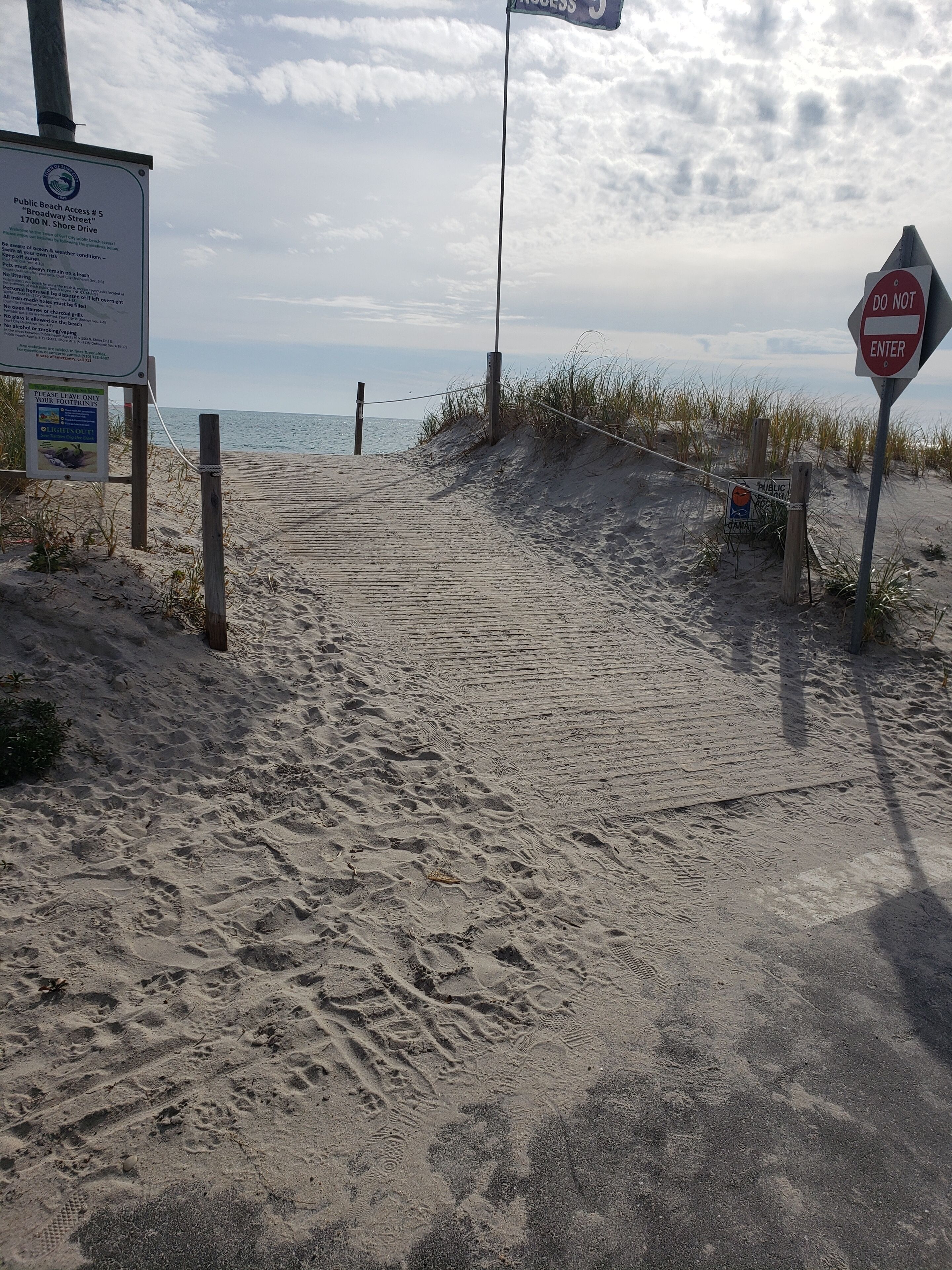 Ein Sandweg am Strand mit einem Schild, das den Zugang zum öffentlichen Strand anzeigt, und einem Verbotsschild.
