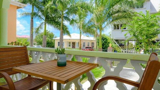 A wooden table and chairs on a balcony with a view of palm trees and a building in the background. - Modern two bedroom, 2 bathroom near Jolly beach for a peaceful stay. (St Mary's Parish)