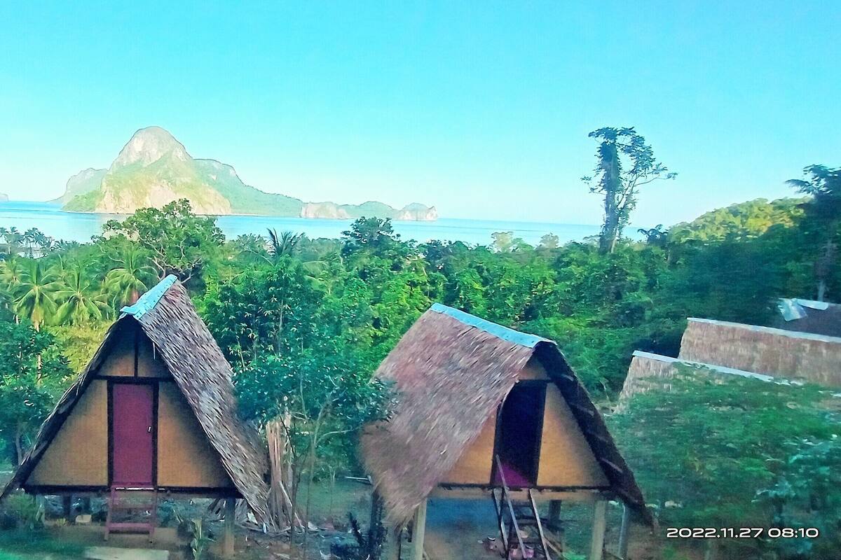 Una hilera de chozas con techo de paja y vistas a una costa montañosa.