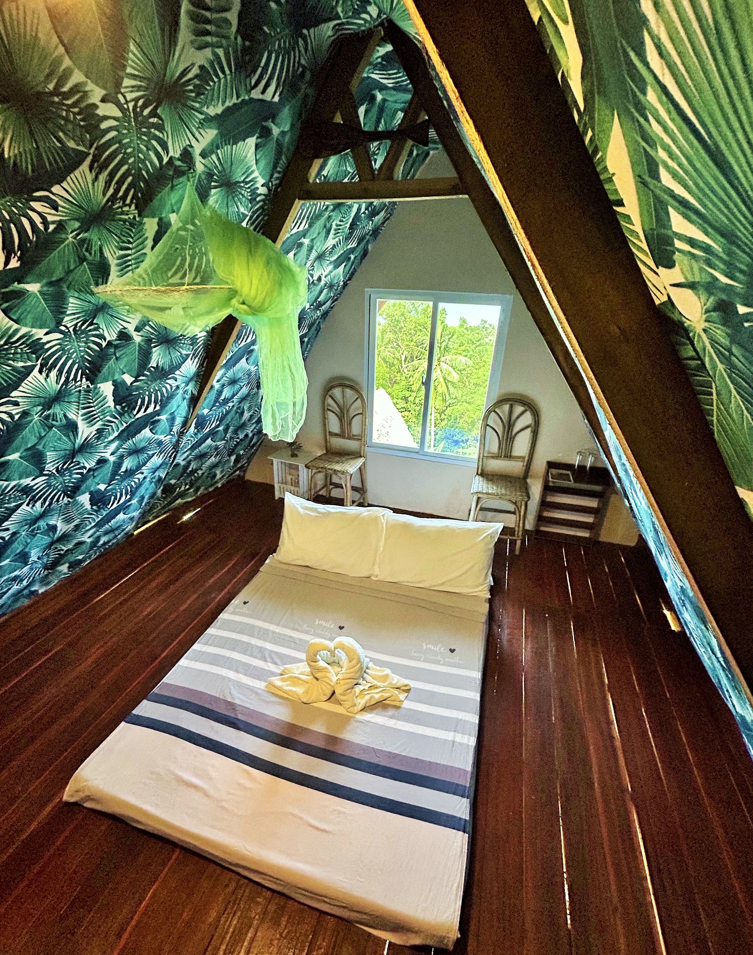 A room with a bed, two chairs, a window, and a view of greenery outside.
