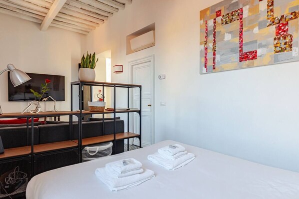 A hotel room with a bed, a desk with a lamp, a TV, a plant, and a wall art piece. - TRASTEVERE CHARMING APARTMENT (Roma)