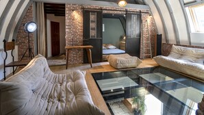 A loft-style bedroom with exposed brick walls, a loft bed, a glass coffee table, and a modern sofa. - La Case à Tom swimming pool, children's playground in Lozère - special discount for July (MENDE)