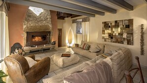 A cozy living room with a stone fireplace, a large sectional sofa, and a decorative wall piece. - La Case à Tom swimming pool, children's playground in Lozère - special discount for July (MENDE)