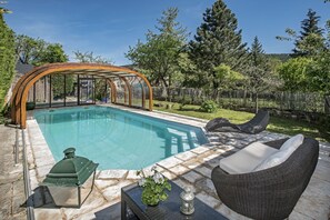 Una piscina con una pérgola de madera, mobiliario exterior y un patio de piedra.