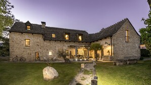 A stone house with a patio, a bicycle, and a large rock in the yard. - La Case à Tom swimming pool, children's playground in Lozère - special discount for July (MENDE)