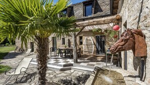 A stone building with a palm tree, outdoor seating, and a horse head sculpture. - La Case à Tom swimming pool, children's playground in Lozère - special discount for July (MENDE)