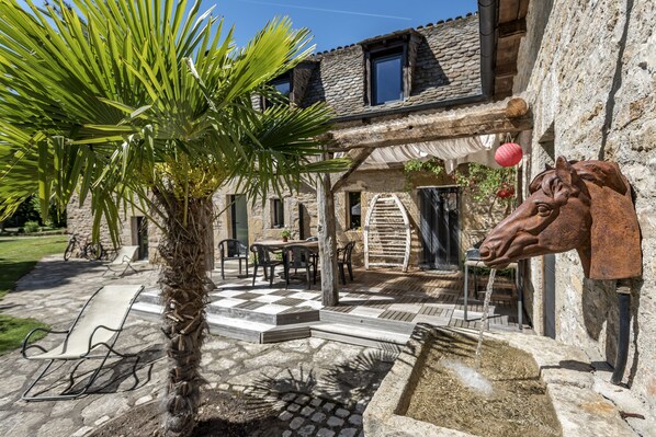Un edificio de piedra con una palmera, mesas al aire libre y una escultura de cabeza de caballo.