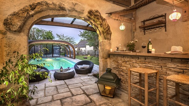 An outdoor patio with stone flooring, a pool, wicker furniture, and a bar area with stools and a lantern. - La Case à Tom swimming pool, children's playground in Lozère - special discount for July (MENDE)