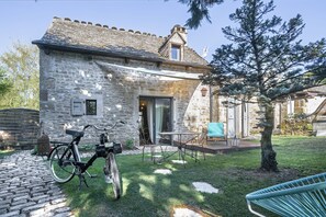 Un edificio de piedra con techo de tejas, una bicicleta, mobiliario exterior y un árbol.
