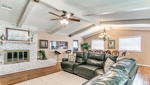A spacious living room with a leather sectional sofa, a fireplace, a ceiling fan, and a dining area visible through an open doorway. - Kindness - Wheelchair Accessible,BOK cent, Expo Sq (Tulsa)