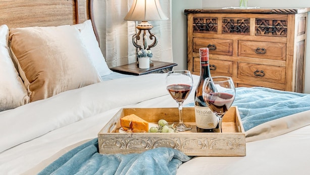A bed with a tray of cheese, grapes, and wine glasses, a bottle of wine, and a decorative lamp. - Kindness - Wheelchair Accessible,BOK cent, Expo Sq (Tulsa)