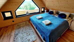 A cozy attic bedroom with a sloped ceiling, a large window, a bed with blue bedding, and a small rug. - Chatka pod Górką by Interhome (Wisla)