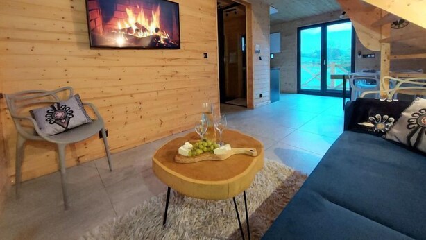 A cozy living room with a wooden interior, a fireplace, a sofa, a dining area, and a staircase. - Chatka pod Górką by Interhome (Wisla)