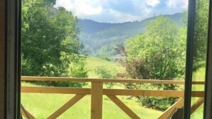 A balcony with a wooden railing, a small table with a glass of wine, and a view of a green landscape with trees and hills. - Chatka pod Górką by Interhome (Wisla)