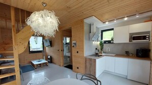 A modern kitchen with white cabinets, a microwave, and a coffee maker. There's a dining table with chairs and a wooden staircase leading to another room. - Chatka pod Górką by Interhome (Wisla)