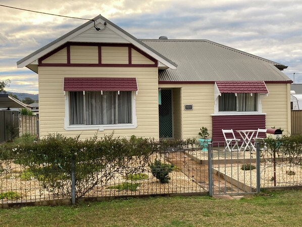 A single-story house with a gabled roof, a front porch with a bench, and a fenced yard. - “Joy” cottage 10km from the Hunter Valley wineries, close to everything. (Cessnock)