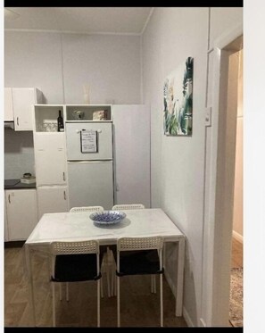 A compact kitchen with white cabinets, a refrigerator, and a dining table with four chairs. - “Joy” cottage 10km from the Hunter Valley wineries, close to everything. (Cessnock)