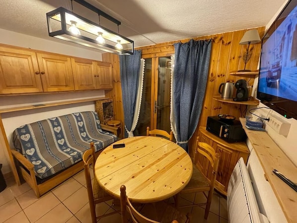 A compact kitchen with wooden cabinets, a round table, and a built-in stove. - Reindeer forest apartment (Villard-sur-Doron)
