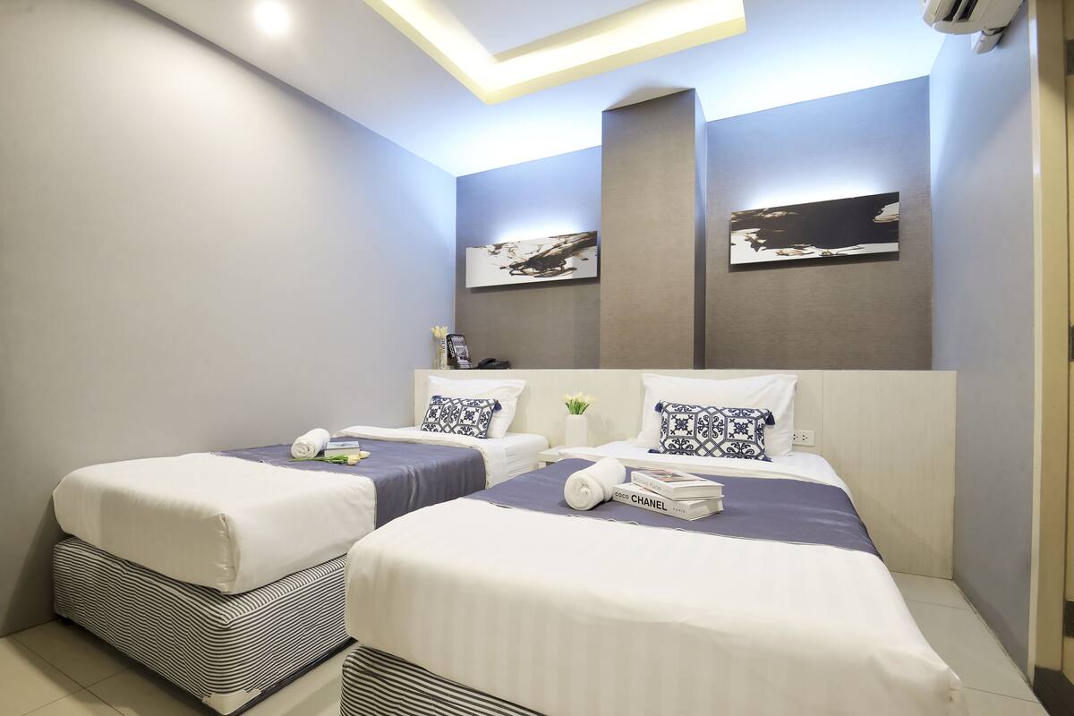 Une chambre d’hôtel moderne avec deux lits, une grande fenêtre et un luminaire au plafond.
