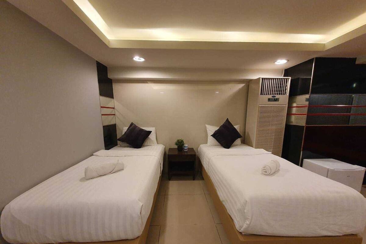 Une chambre d’hôtel avec deux lits simples, une petite table, une table de chevet et un système de climatisation intégré.