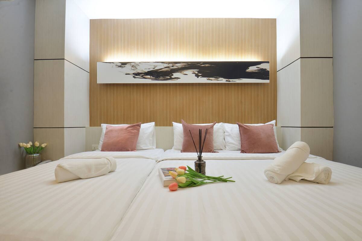 Une chambre d’hôtel avec un grand lit, une tête de lit ornée d’un tableau et un vase rempli de fleurs.
